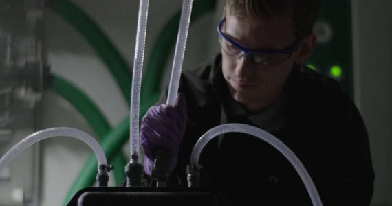 Person wearing safety goggles and gloves adjusts tubing and equipment in a laboratory setting.